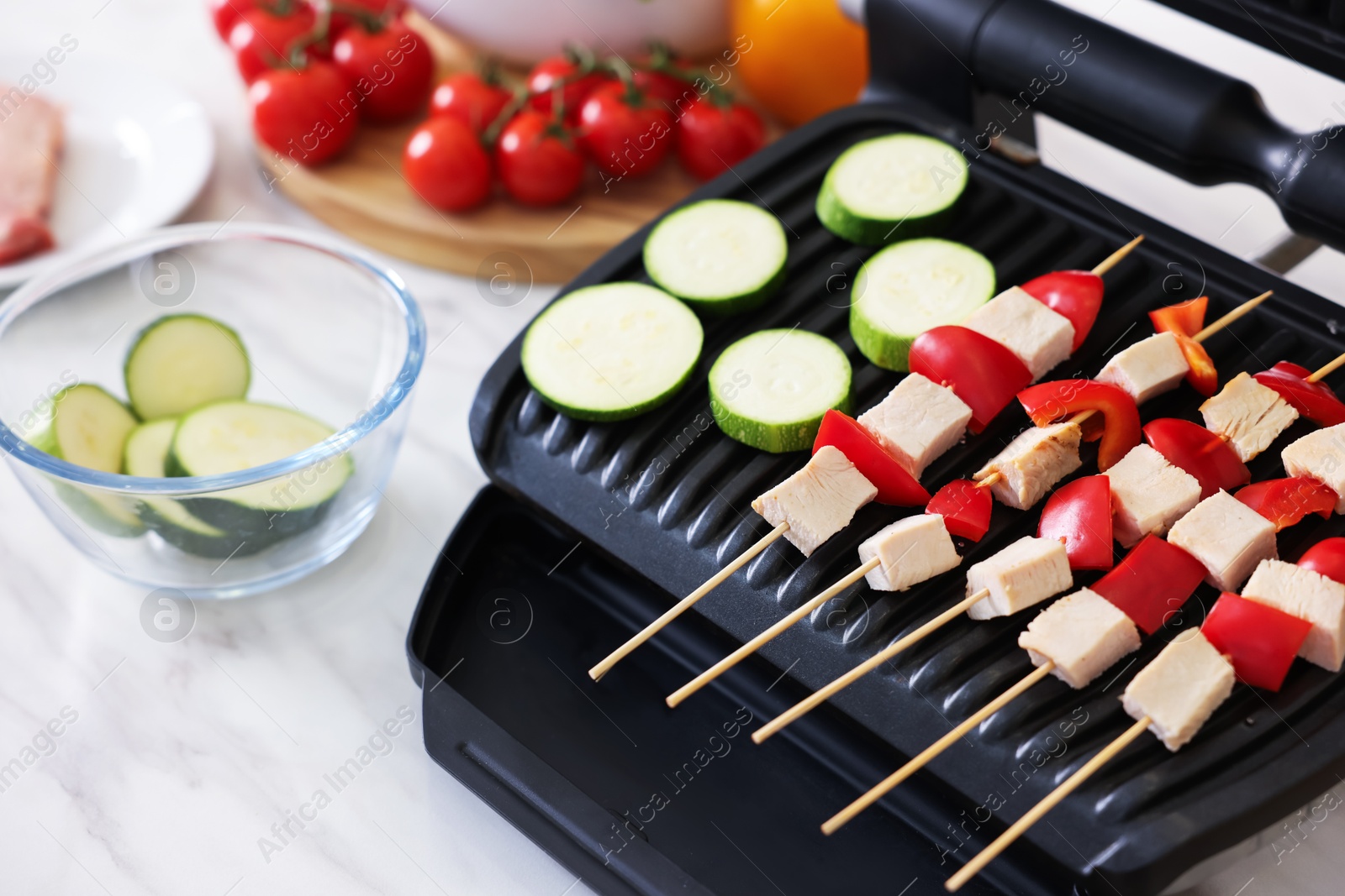 Photo of Woman cooking skewers with meat and vegetables on electric grill at home, closeup