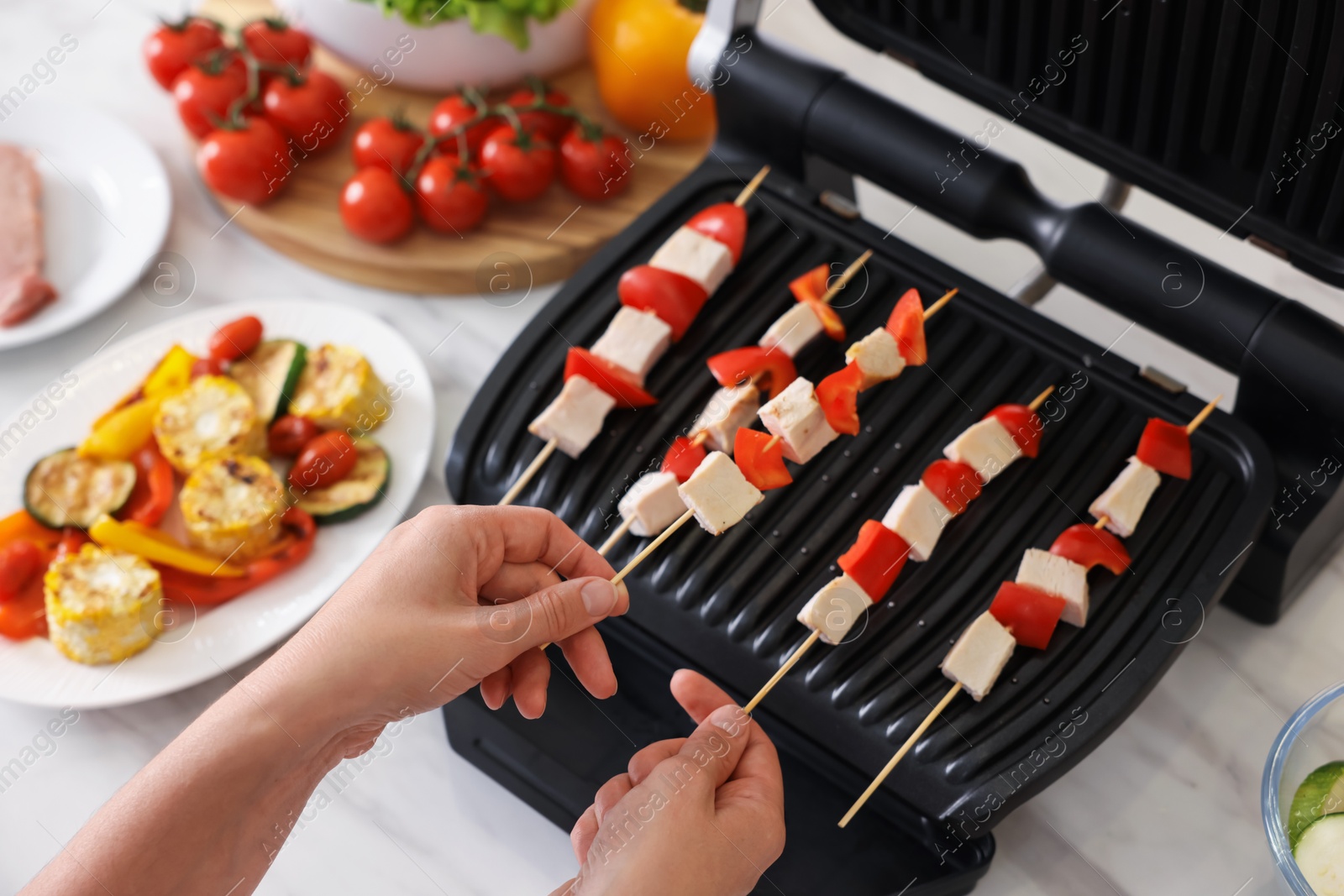 Photo of Woman cooking skewers with meat and vegetables on electric grill at home, closeup