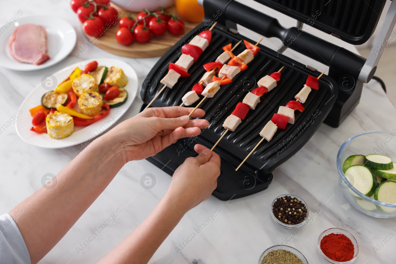 Photo of Woman cooking skewers with meat and vegetables on electric grill at home, closeup