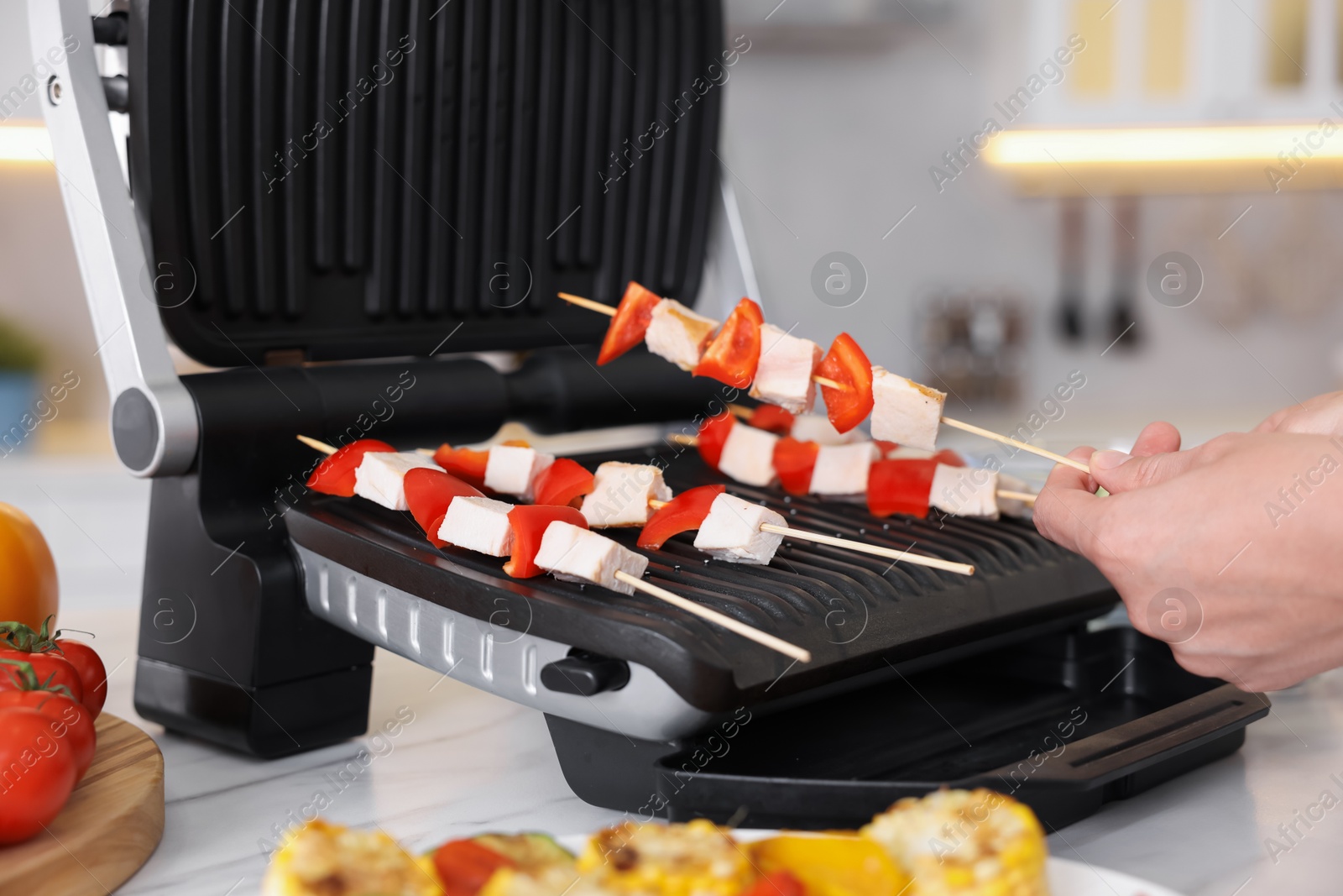Photo of Woman cooking skewers with meat and vegetables on electric grill at home, closeup