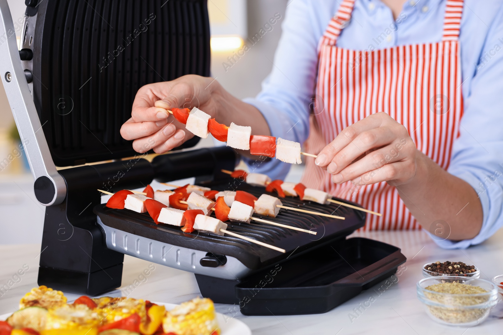 Photo of Woman cooking skewers with meat and vegetables on electric grill at home, closeup