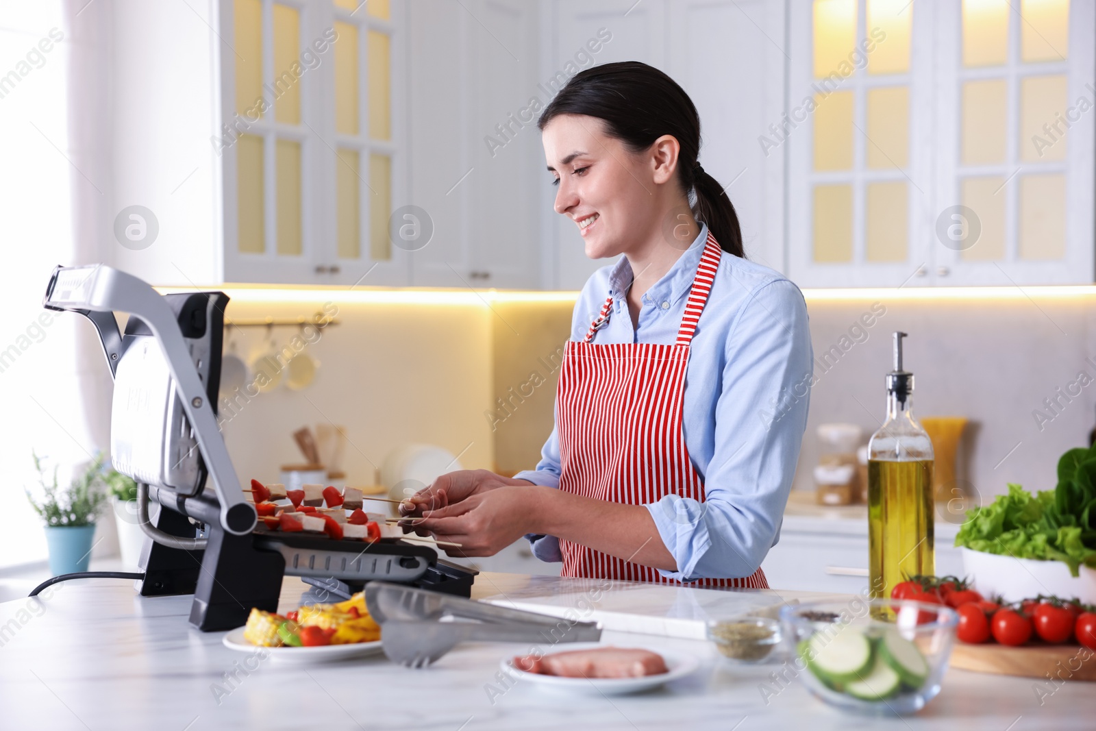Photo of Woman cooking skewers with meat and vegetables on electric grill at home