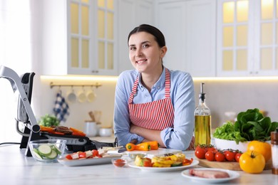 Photo of Woman cooking vegetables and meat on electric grill in kitchen