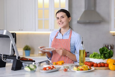 Photo of Woman cooking vegetables and meat on electric grill in kitchen