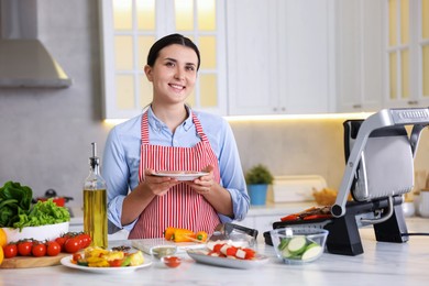 Photo of Woman cooking vegetables and meat on electric grill in kitchen