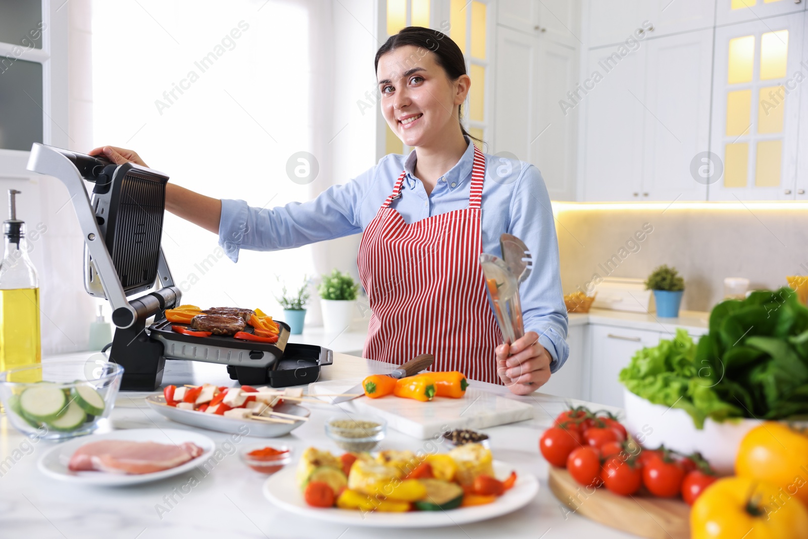 Photo of Woman cooking vegetables and meat on electric grill in kitchen
