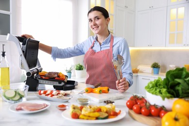 Photo of Woman cooking vegetables and meat on electric grill in kitchen