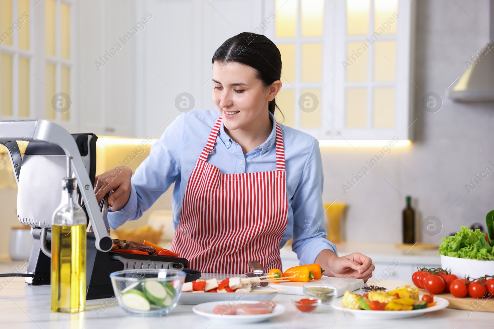Photo of Woman cooking vegetables and meat on electric grill in kitchen