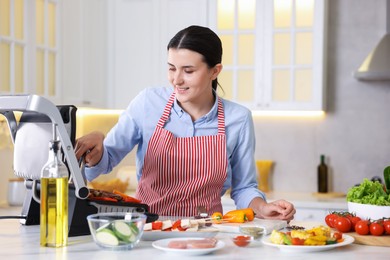 Photo of Woman cooking vegetables and meat on electric grill in kitchen