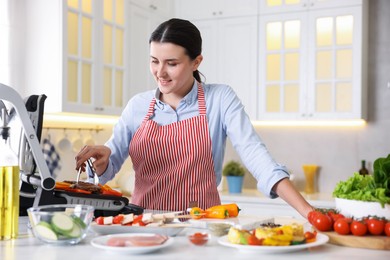 Photo of Woman cooking vegetables and meat on electric grill in kitchen