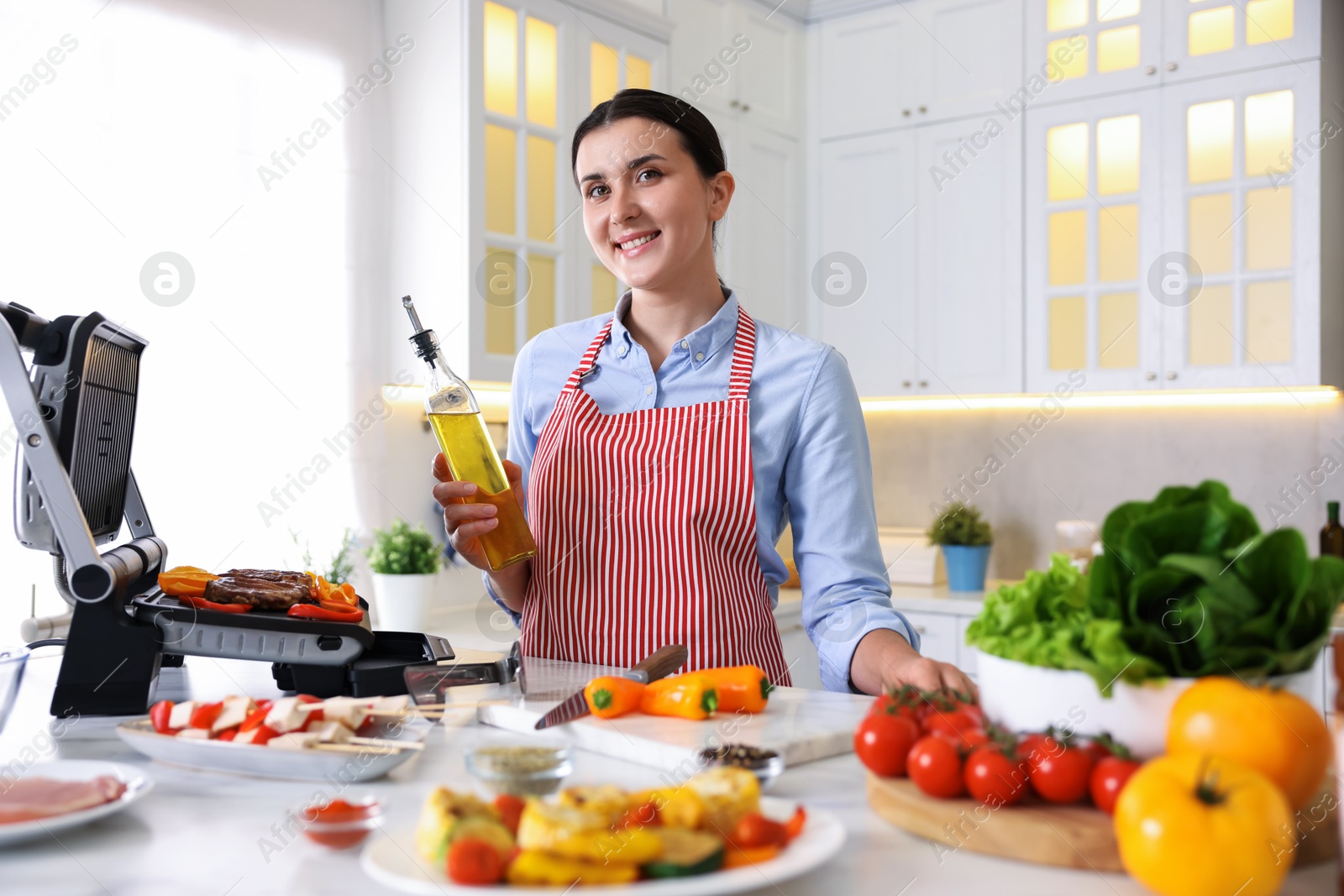 Photo of Woman cooking vegetables and meat on electric grill in kitchen