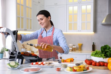 Photo of Woman pouring oil onto vegetables cooking on electric grill in kitchen