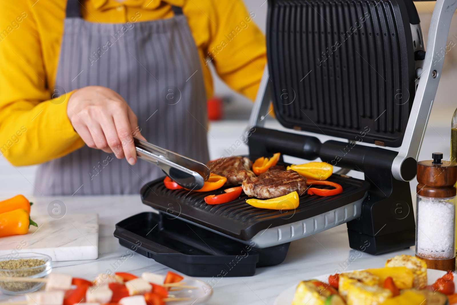 Photo of Woman cooking vegetables and meat on electric grill in kitchen, closeup
