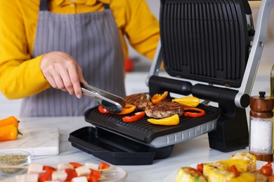 Photo of Woman cooking vegetables and meat on electric grill in kitchen, closeup