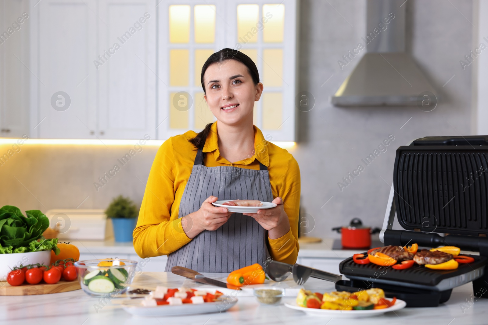 Photo of Woman cooking vegetables and meat on electric grill in kitchen