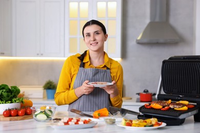 Photo of Woman cooking vegetables and meat on electric grill in kitchen