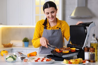 Photo of Woman cooking vegetables and meat on electric grill in kitchen