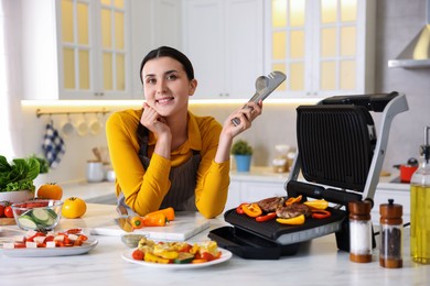 Photo of Woman cooking vegetables and meat on electric grill in kitchen