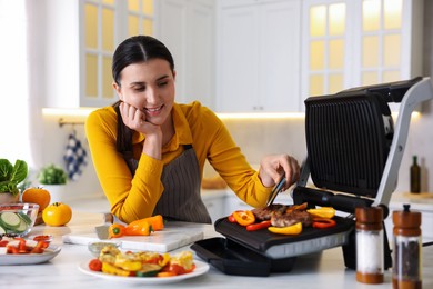 Photo of Woman cooking vegetables and meat on electric grill in kitchen
