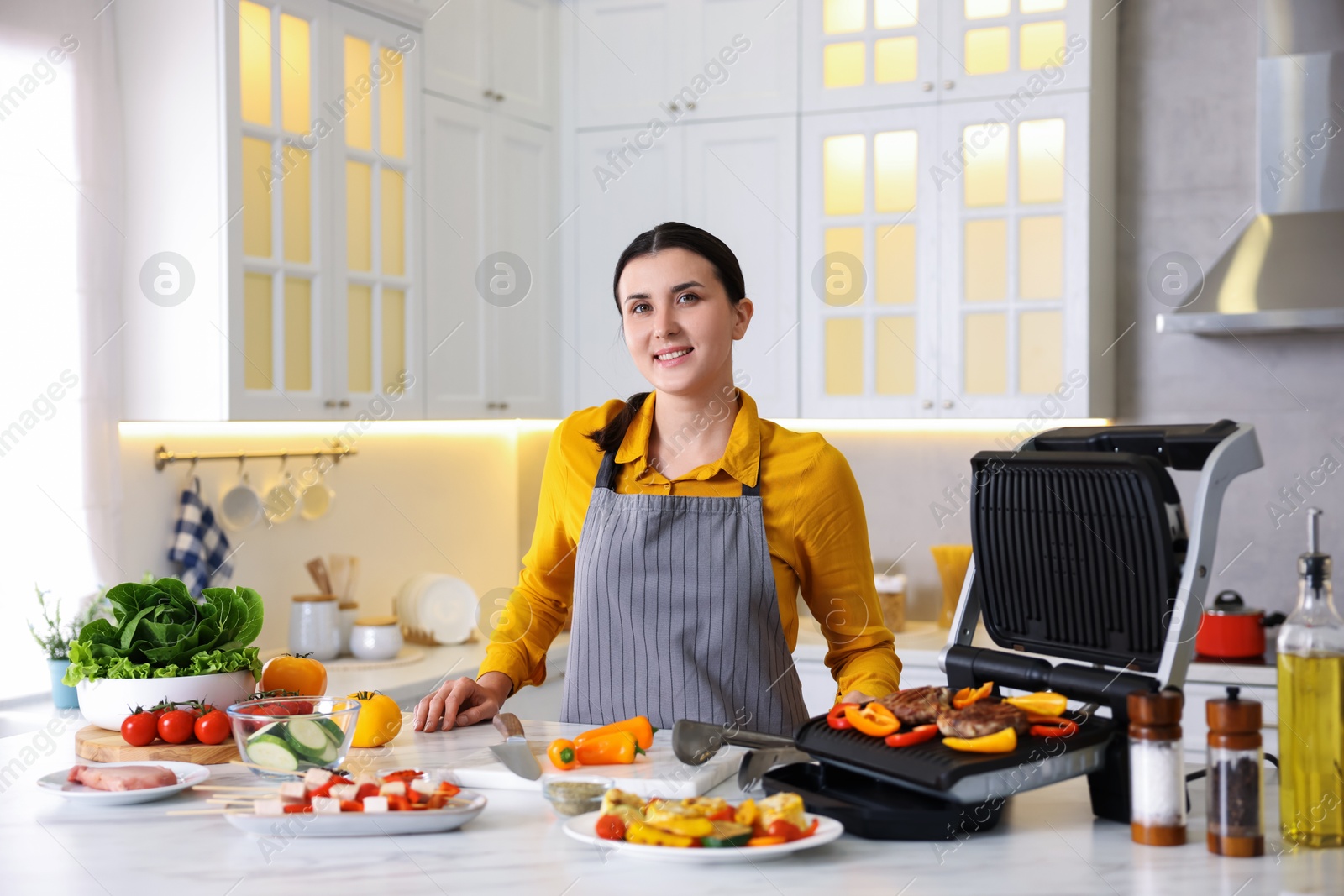 Photo of Woman cooking vegetables and meat on electric grill in kitchen