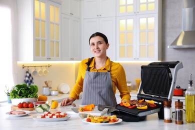 Photo of Woman cooking vegetables and meat on electric grill in kitchen