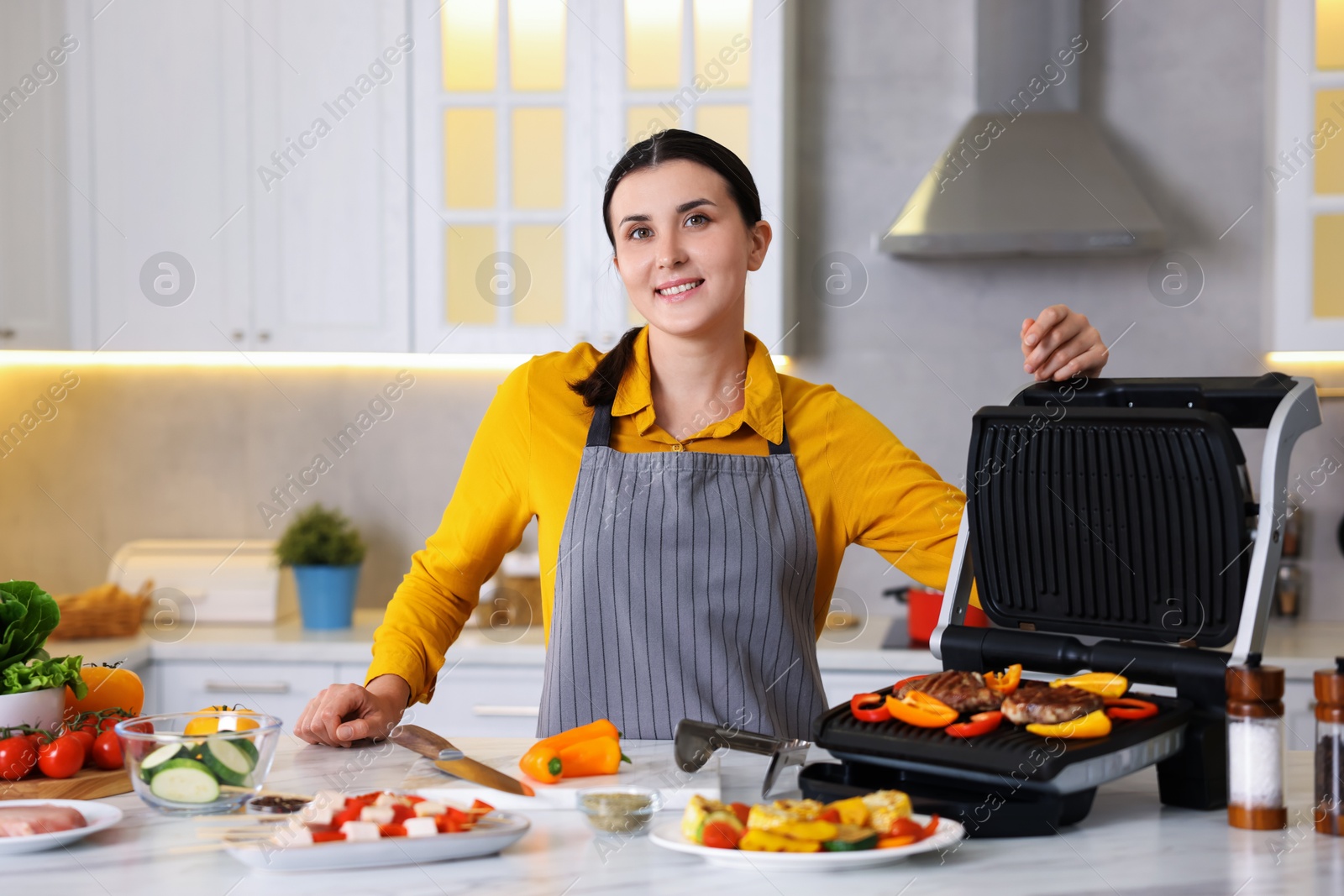 Photo of Woman cooking vegetables and meat on electric grill in kitchen