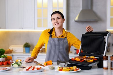 Photo of Woman cooking vegetables and meat on electric grill in kitchen