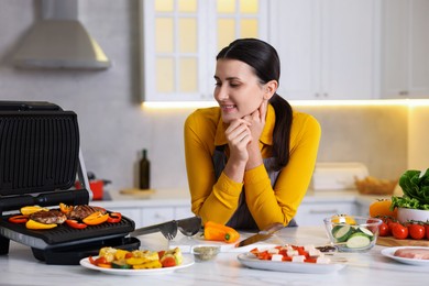 Photo of Woman cooking vegetables and meat on electric grill in kitchen