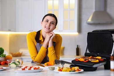Photo of Woman cooking vegetables and meat on electric grill in kitchen