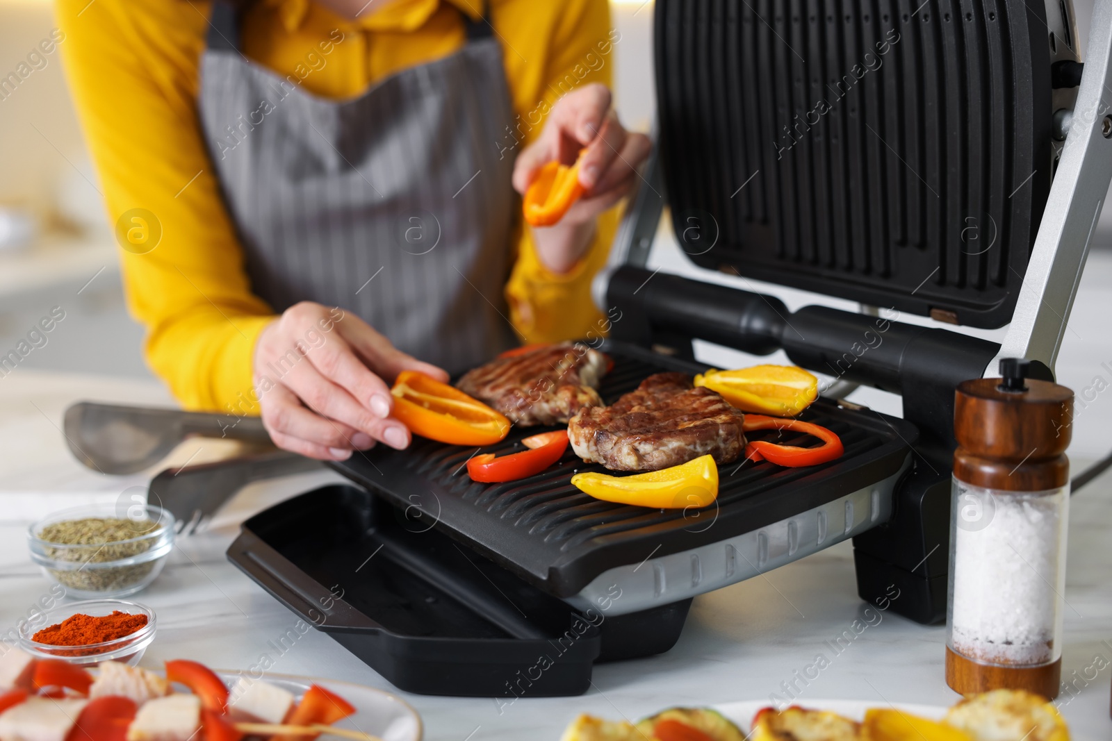 Photo of Woman cooking vegetables and meat on electric grill in kitchen, closeup