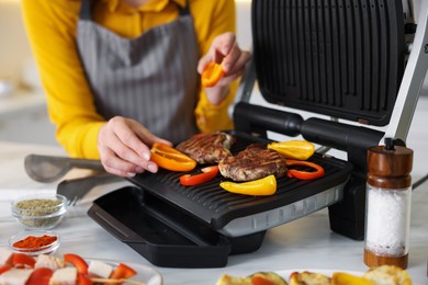 Photo of Woman cooking vegetables and meat on electric grill in kitchen, closeup