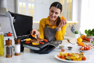 Photo of Woman cooking vegetables and meat on electric grill in kitchen