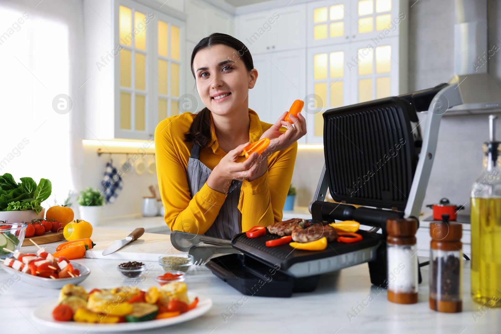 Photo of Woman cooking vegetables and meat on electric grill in kitchen