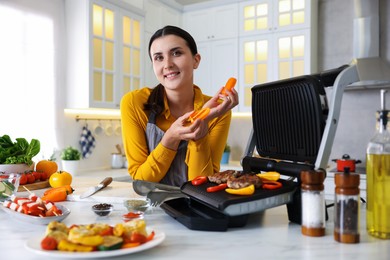 Photo of Woman cooking vegetables and meat on electric grill in kitchen