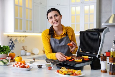 Photo of Woman cooking vegetables and meat on electric grill in kitchen