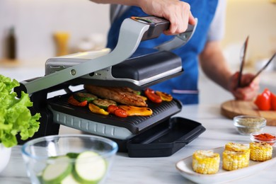 Photo of Man cooking vegetables and meat on electric grill in kitchen, closeup