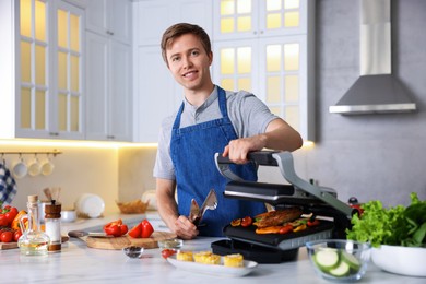 Photo of Man cooking vegetables and meat on electric grill in kitchen