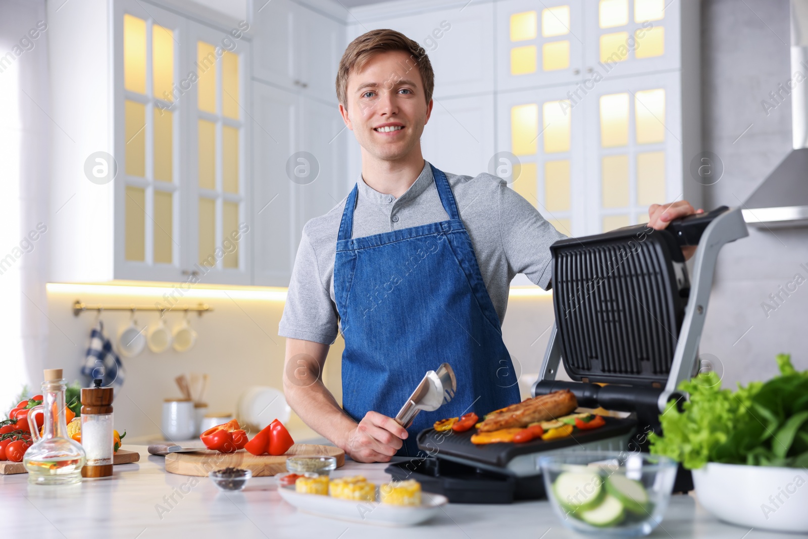Photo of Man cooking vegetables and meat on electric grill in kitchen
