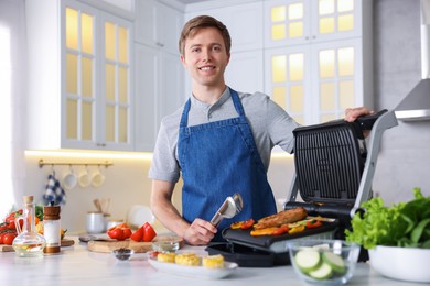 Photo of Man cooking vegetables and meat on electric grill in kitchen