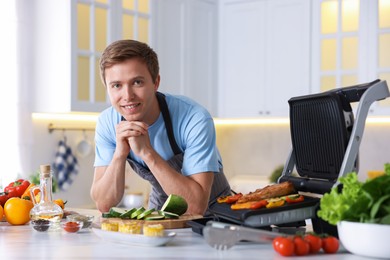 Photo of Man cooking vegetables and meat on electric grill in kitchen