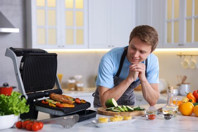 Photo of Man cooking vegetables and meat on electric grill in kitchen