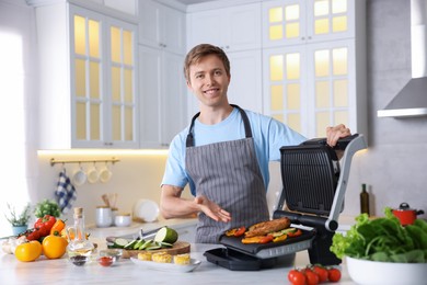 Photo of Man cooking vegetables and meat on electric grill in kitchen