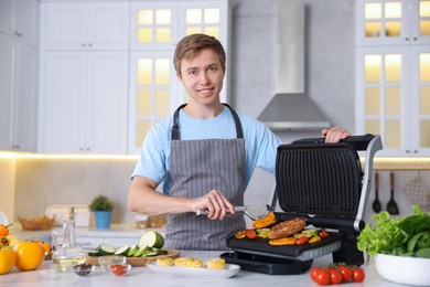 Photo of Man cooking vegetables and meat on electric grill in kitchen