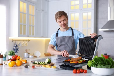 Photo of Man cooking vegetables and meat on electric grill in kitchen