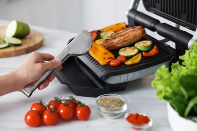 Photo of Man cooking vegetables and meat on electric grill in kitchen, closeup