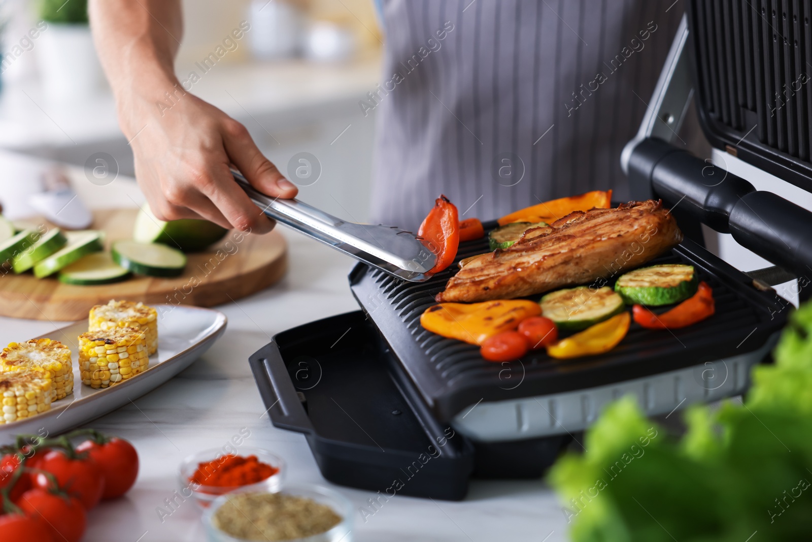 Photo of Man cooking vegetables and meat on electric grill in kitchen, closeup