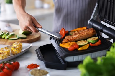 Photo of Man cooking vegetables and meat on electric grill in kitchen, closeup