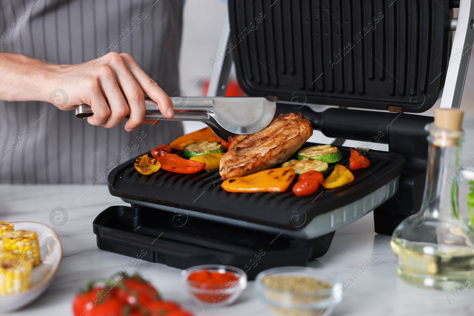Photo of Man cooking vegetables and meat on electric grill in kitchen, closeup