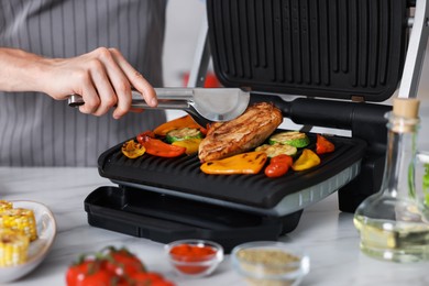 Photo of Man cooking vegetables and meat on electric grill in kitchen, closeup