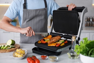 Photo of Man cooking vegetables and meat on electric grill in kitchen, closeup